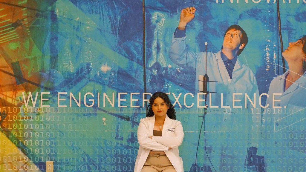 CIRM Bridges student Esme Ruiz-Garcia posing in front of a mural that says "we engineer excellence" at California State University, San Bernadino.