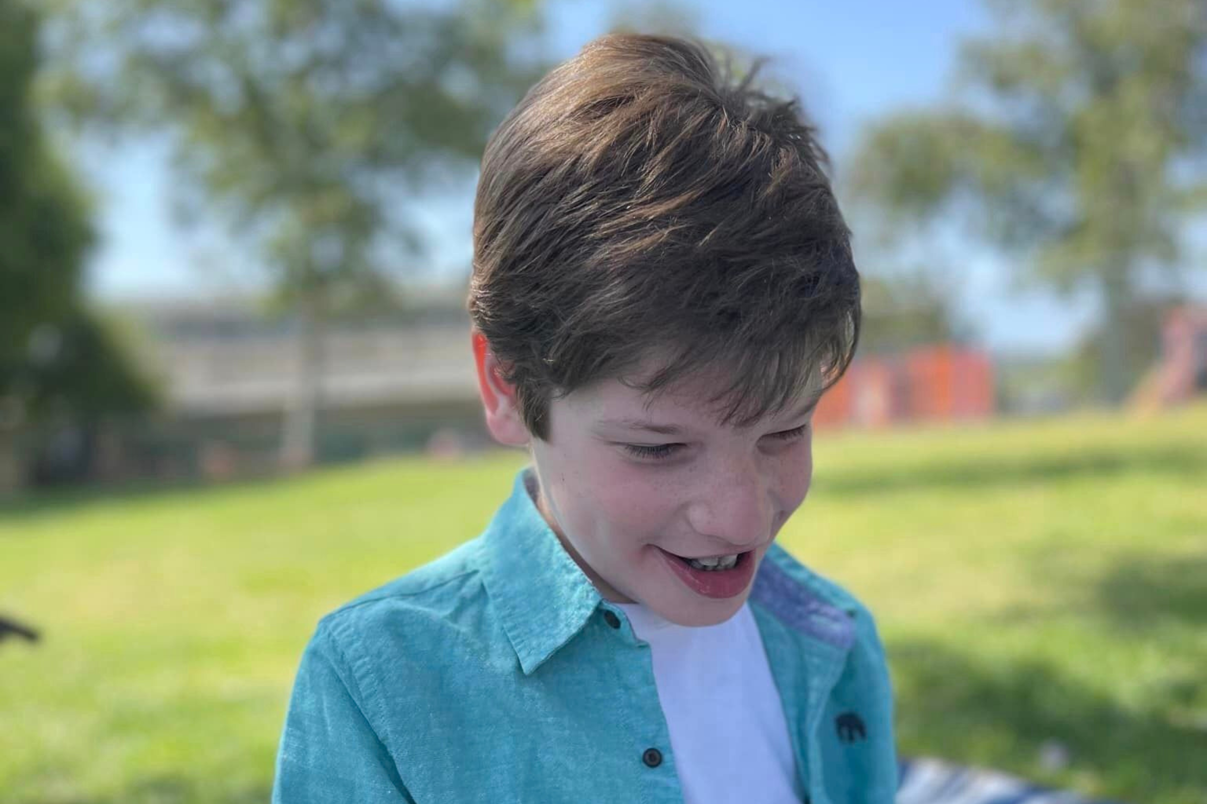 Young boy outside smiling and looking down