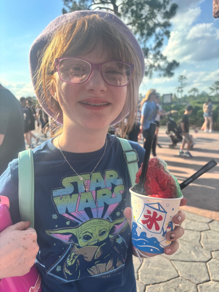 Close up of a young girl with glasses. She has a big smile on her face and a snow-cone in her left hand.